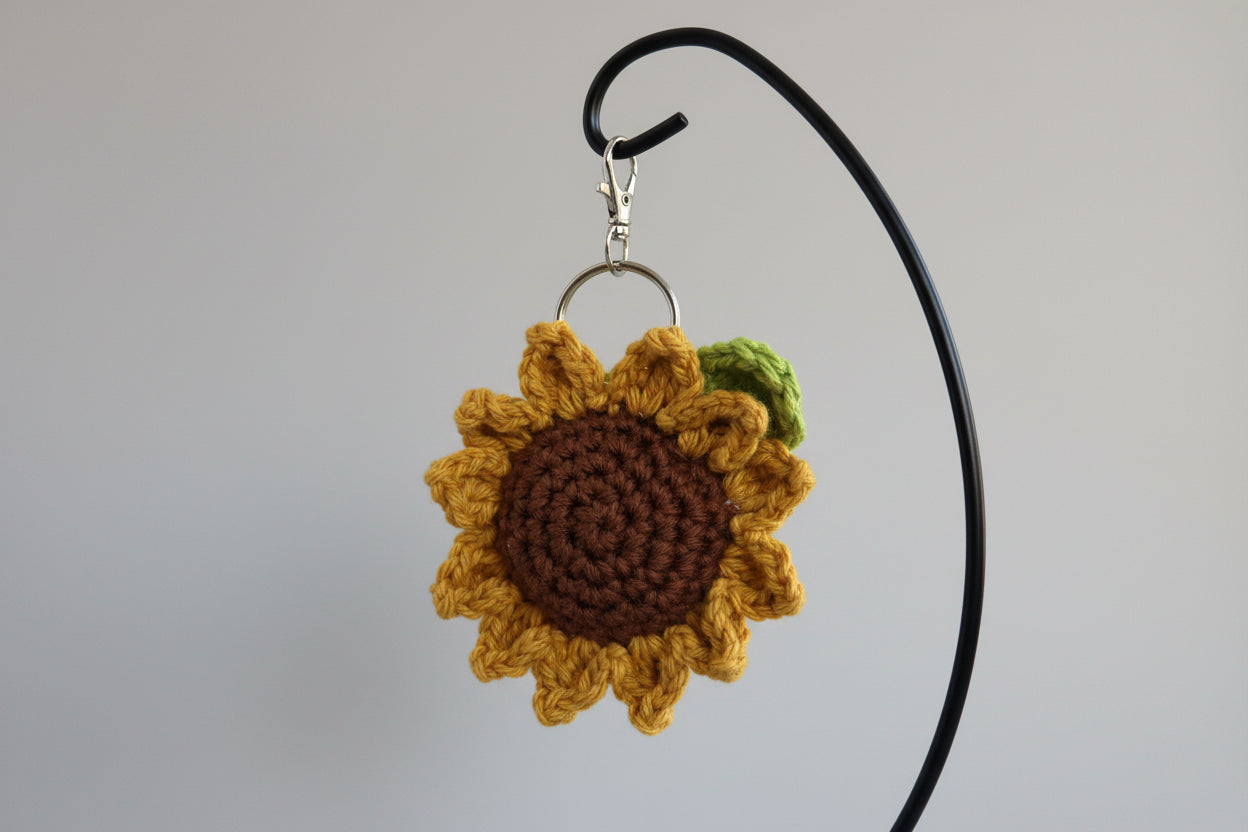 Crocheted sunflower keychain on a hook against a light blue wall.