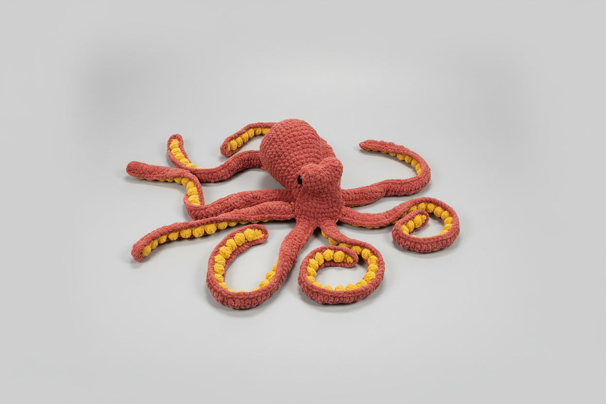 Crocheted octopus toy with red body and yellow suction cups on a gray surface