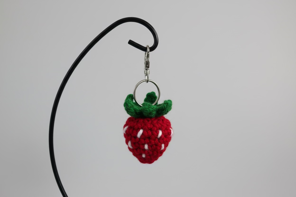 Crocheted strawberry keychain on a black cord against a light blue background