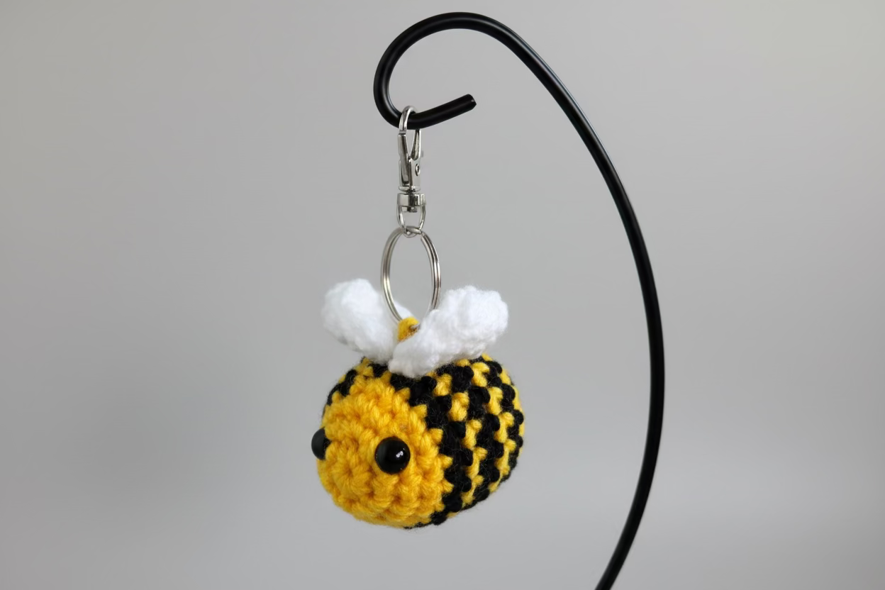 Crocheted bee keychain on a hook against a light blue wall.