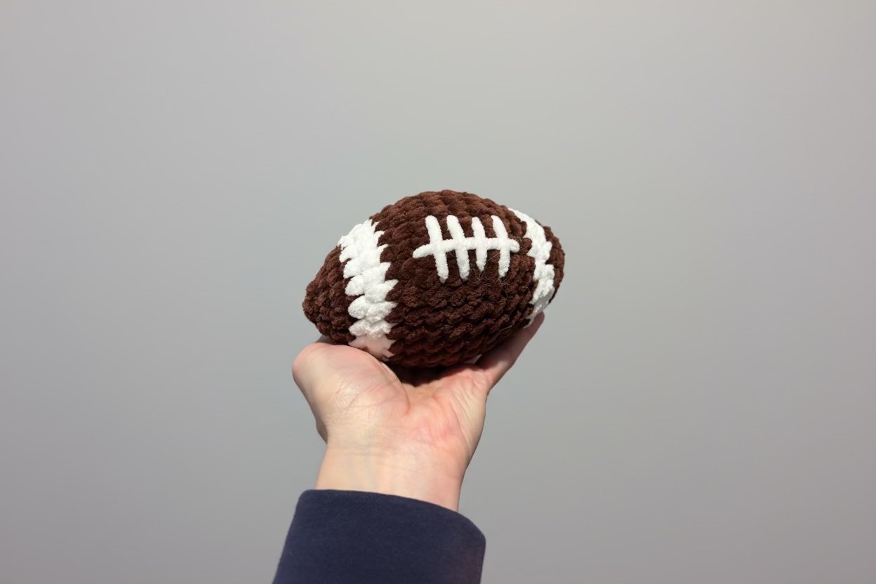 Hand holding a crochet football against a stone wall background
